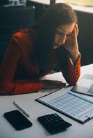 Portrait of tired young business Asian woman work with documents tax laptop computer in office. Sad, unhappy, Worried, Depression, or employee life stress concept photo