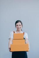 Smiling Asian woman in casual clothes holding a cardboard box mockup while standing against an isolated white background. shipping business concept photo