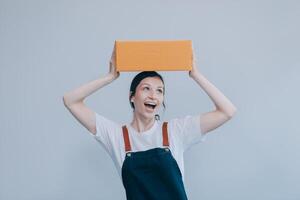 Smiling Asian woman in casual clothes holding a cardboard box mockup while standing against an isolated white background. shipping business concept photo