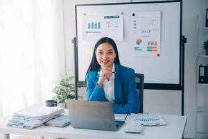 Cheerful business lady working on laptop in office, Asian happy beautiful businesswoman in formal suit work in workplace. Attractive female employee office worker smile. photo