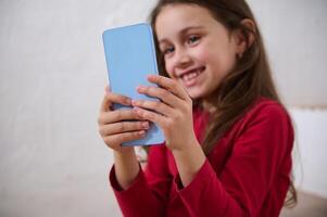 moderno inteligente móvil teléfono en el manos de un borroso sonriente pequeño niño chica, un digital fanático niño hojeada sitios web, jugando en línea juegos, acecho bloggers o dibujos animados en Internet. foto