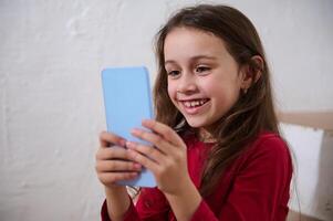 Close-up portrait of a smiling happy child having fun on smart mobile phone, using mobile apps, playing online games or watching movies webinars or kids bloggers, isolated white background photo