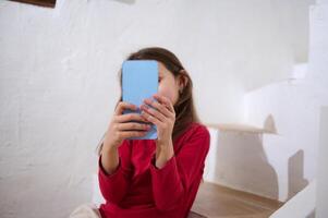 Details on a blue smartphone in the child's hands. Elementary age kid girl using smartphone, browsing mobile app, social media content, watch cartoons on internet, online chat communication, have fun photo