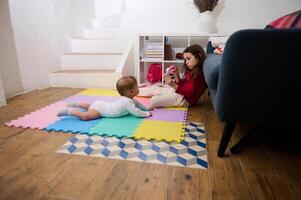 lado retrato de un linda pequeño niño chica, amoroso cuidando hermana jugando con su bebé chico hermano en un vistoso rompecabezas alfombra a acogedor hogar interior. niños. contento familia y mundo para niños día concepto foto