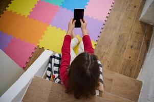 View from above of kid's hands holding smart mobile phone with blank black empty digital touch screen. Mockup. Copy space for mobile application or advertising text. People. Wireless technology photo