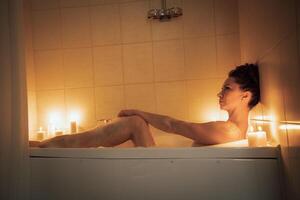 A woman is sitting in a bathtub with candles lit around her. Scene is relaxing and calming. photo