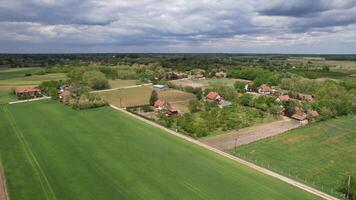 Aerial view of a tranquil rural village surrounded by green fields under a cloudy sky, ideal for themes of agriculture, sustainability, and rural living video