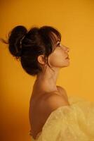 Profile portrait of a beautiful middle-aged woman in a yellow dress, her hair pulled up against a yellow background photo