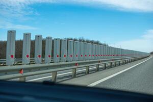 A road with a long line of metal posts with red hearts on them. The road is empty and the sky is clear. photo