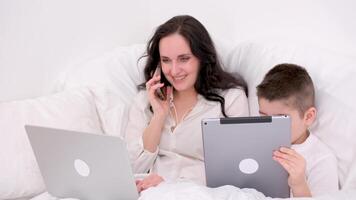 Arbeit beim Zuhause online Mama und Sohn sitzen im Bett Laptop Tablette Telefon Lektionen online Arbeit Frau reden Telefon lächelnd Herstellung bestellen löst Geschäft Probleme Intimität Liebe Single Mutter Arbeit ist aus von das Büro video