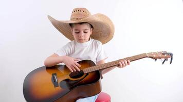 con fiducia detiene un' chitarra nel il suo mani su cappello giochi un' chitarra su un' bianca sfondo riposo rilassamento un' musicale strumento memorizzare un' capi di abbigliamento memorizzare per bambini copricapo scuola materna tempo per scuola video