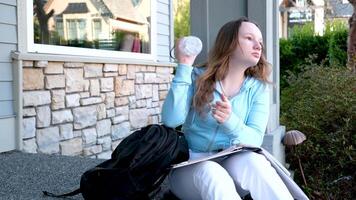 portrait de femme en portant une bouteille de l'eau et boire, portant école uniforme et bleu sac à dos asseoir sur le sol contre le gris mur video