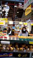 3 Mädchen im Masken von Asien verkaufen Gemüse und Früchte auf das Zähler ein alt Frau von Pensionierung Alter Spaziergänge Vergangenheit Sie sie sieht aus und Blätter video