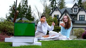 adolescenti mostrare Pizza fette pollici su Pizza consegna gioventù persone seduta su picnic mangiare Pizza nel sfondo nel primo piano il computer portatile con vuoto schermo sta su bianca scatole con consegna estate marketing video