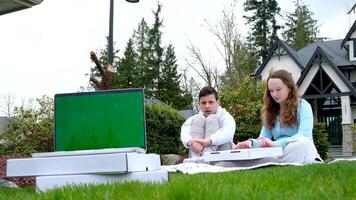 snabb färsk pizza leverans ungdom ung bror och syster Sammanträde på picknick äter pizza i bakgrund i förgrund bärbar dator med tom skärm står på vit lådor med leverans sommar marknadsföring video