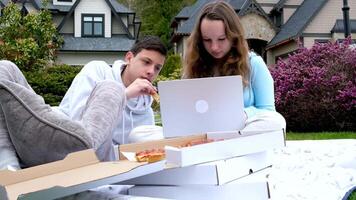 online Lernen draußen Jungs Mädchen Sitzung Gadget draußen Picknick Essen Pizza Lernen Lektionen mit ein Laptop im Hände freunde Klassenkameraden Bruder und Schwester aussehen zum ein gut Film lösen Probleme video