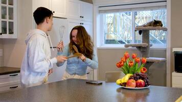 Happy teenages having fun dancing in kitchen. Smiling girl teaching teen boy to wash showing dance before cooking or eating enjoying family life together at home. video