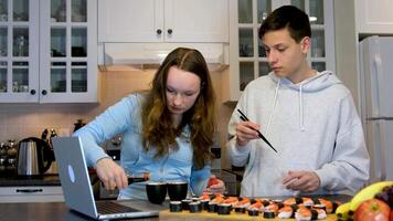 har roligt Tonårs pojke och flicka tittar på film på bärbara datorer äter sushi i kök mat leverans snabb mat roligt tidsfördriv trevlig relation först datum vänner klasskamrater tillsammans bror och syster video