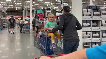 mother with three children going grocery shopping children sitting in shopping cart girl picking up t-shirt playing lot of people in large supermarket for weekend passing by slow large selection video