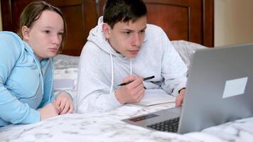 Garoto menina assistindo conectados lição sentado perto computador gêmeos irmão e irmã estude dentro mesmo classe Garoto segurando caneta escreve baixa importante em formação ser às casa quarentena assistindo Inglês cursos video