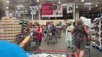 Costco Wholesale shopping in a huge supermarket people walking by with carts choosing goods high ceilings in the store different food on the counter rushing women and men wholesale America Canada video