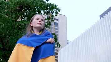 a beautiful Ukrainian woman in an embroidered holds Ukrainian flag on the background of the house a tree dreams of victory protection asks for help sad eyes fair hair confident strong imperious look video