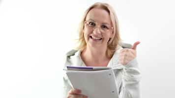 pouce en haut femme avec des lunettes en riant blond en train de lire une blanc bloc-notes sur une lumière Contexte sincère sourire écrire vers le bas des idées viens en haut avec l'intérêt La publicité les propositions écrire une livre video