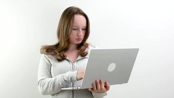 Image of a young blonde woman sitting on a white surface with a laptop in her lap. video