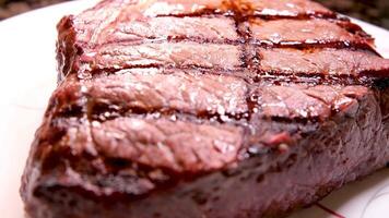 gegrild t-bone steak geserveerd Aan wit bord in vlees restaurant, gefilmd van bovenstaand met zoom uit effect.sluiten omhoog klem van rundvlees stuk gegrild met peper, rozemarijn kruid voor avondeten maaltijd in diner cafe video