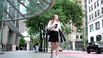 Canadá Vancouver 05.05.2024 Adolescente niña caminando mediante centrar con lululemon paquetes ligero ropa zapatillas la carretera rascacielos suelto marrón pelo europeo viaje comprar regalos teléfono en mano video