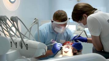 närbild ansikte manlig tandläkare svart mask hans ansikte arbete. kirurg sågar ben, utför drift med sjuksköterska, assistent. tandläkare kirurg nitril handskar tar bort komplex visdom tand. kirurg sågning ben. manlig video