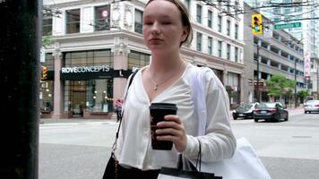 Canada Vancouver 05.05.2024 tiener- meisje wandelen door centrum met slaapliedje pakketjes licht kleren sportschoenen weg wolkenkrabbers los bruin haar- Europese reizen kopen cadeaus telefoon in hand- video