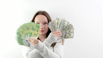 rich teenager girl waving a fan of 100 euros and 100 dollar bills standing on a white background smiling in a sports gray sweater loose brown hair surprise calm rich child video