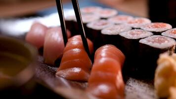 composición de diferente tipos de Sushi rollos metido en negro Roca tablero. palillos y soja salsa cuenco en lado. parte superior ángulo vista. video