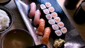 composizione di diverso tipi di Sushi rotoli posto su nero pietra tavola. bastoncini e soia salsa ciotola su lato. superiore angolo Visualizza. video