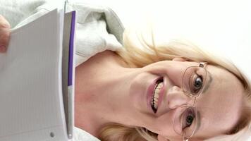 thumb up woman with glasses laughing blonde reading a white notepad on a light background sincere smile write down ideas come up with interest advertising proposals write a book video