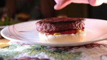 plaats een groot rundvlees pasteitje Aan een barbecue rooster belegd broodje druk op met uw vinger mosterd saus en ketchup stromen uit van onder de vlees bereiden een Hamburger video