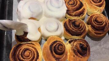 Pouring frosting on Freshly baked cinnamon rolls or Cinnabon close up. Sweet cream cheese frosting pouring on cinnamon rolls. Production of cinnamon rolls. Bakery products. Appetizing cinnamon buns video