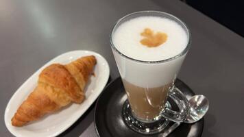 une français croissant et une tasse de cappuccino sur une noir plaque. fermer avec lent mouvement. rotation dans une cercle. blanc Contexte. video