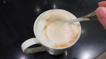 dichtbij omhoog van roeren cappuccino met dik melk schuim hand- roert ochtend- koffie de lepel video