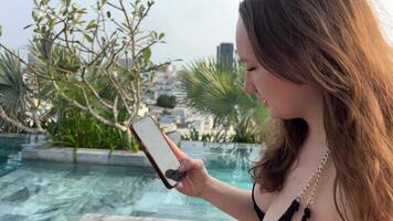 Woman freelancer sits on deck chair near pool and works on laptop. Girl uses laptop for remote work on vacation and receives good news by email video