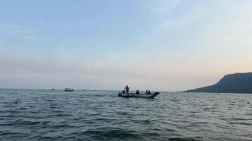 estoque cenas cauda longa barco chegando para a costa silhueta símbolo. contra a fundo do uma tropical pôr do sol silhuetas do jovem homens em a barco, a oceanos, a movimento, água, natureza video