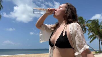 Wasser Balance es ist gierig zu trinken Wasser und verschütten es Anzeige schick Luxus Strand Porträt Frau trinken Wasser von Glas drinnen. Sonnenschein. Stand im Zimmer. lächelnd. Wasser Gleichgewicht. Gesundheit. schleppend Bewegung video