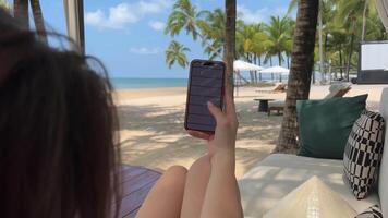 giovane donna utilizzando inteligente Telefono su amaca, dire bugie fra palma alberi nel tropicale clima- persone viaggio vacanze tecnologia su il partire concetto video