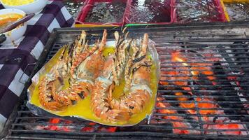 Giant grilled lobster cook on charcoal stove at Thai street food night market. Lobster with flavored butter. Delicious healthy food closeup served for lunch in modern gourmet cuisine restaurant video