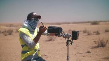 une cameraman dans une réfléchissant gilet est en train de regarder le tournage dans le désert. film tournage. camions qui passe par video
