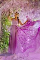 Woman wisteria lilac dress. Thoughtful happy mature woman in purple dress surrounded by chinese wisteria photo