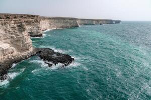 el Oceano es calma y el orilla es rocoso. el agua es un profundo azul color. el rocas son dentado y el olas son pequeño. el escena es pacífico y sereno. foto