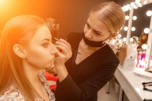 Make-up artist paints eyebrow pencil to beautiful brunette in be photo