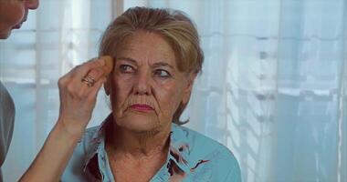 era inventar. aplicando creme com uma esponja para a 85 anos mulher com azul olhos. 4k video